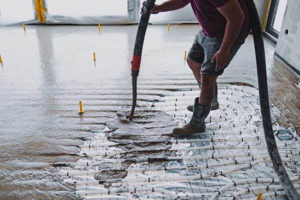 Construction worker pouring concrete over underfloor heating pipes, creating a smooth and level concrete surface